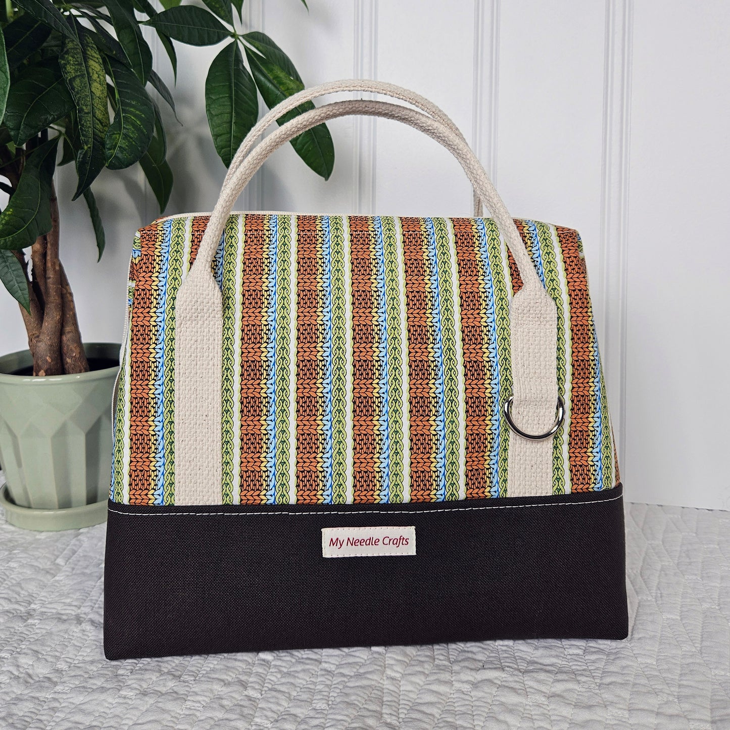 Doctor style knitting bag has brown canvas bottom paired with an orange blue green knit stitch print top. It has natural cream cotton webbing strap handles.