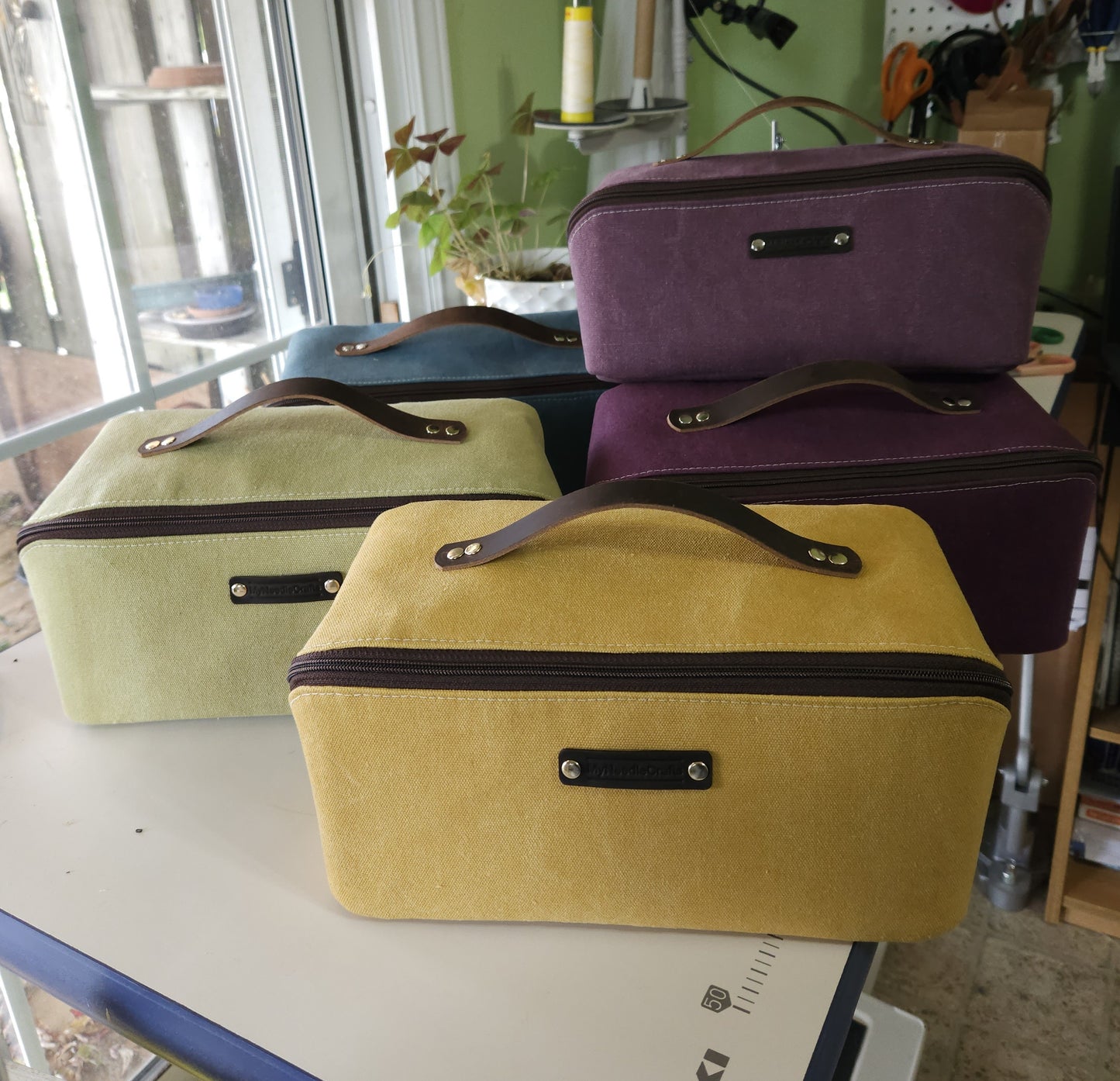 Three fabric knitting cases in yellow, green, blue, and purple on a table with a room background.